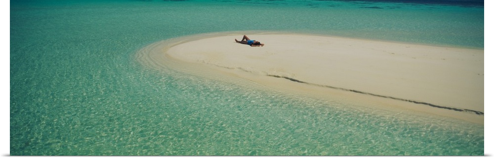 Panoramic photograph of girl tanning on sand bar surrounded by crystal clear ocean.