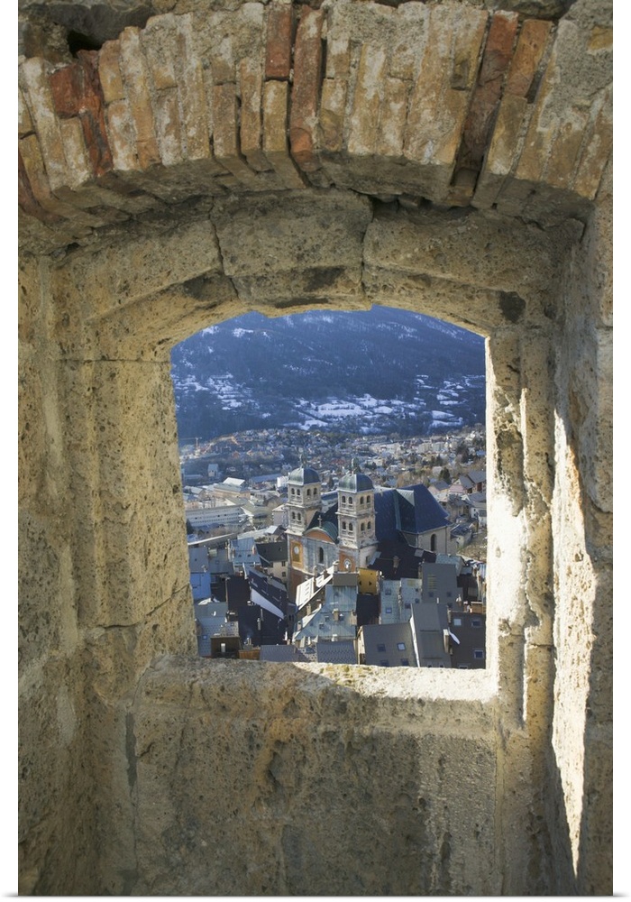 A photograph is taken through a small stone edged window of a town below.