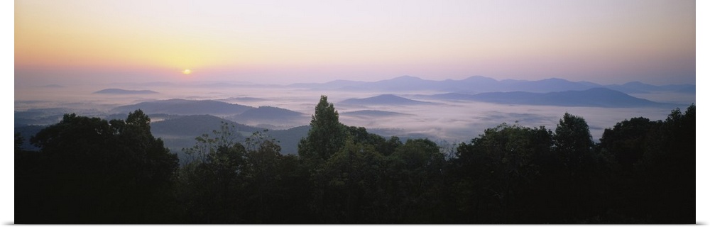 Large panoramic photograph of mountains in Virginia with the sun setting far in the distance and a layer of fog over the m...
