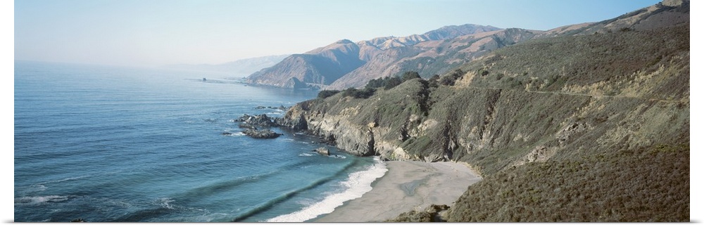 Panoramic image of the Pacific Ocean meeting rocky cliffs and a smooth beach.