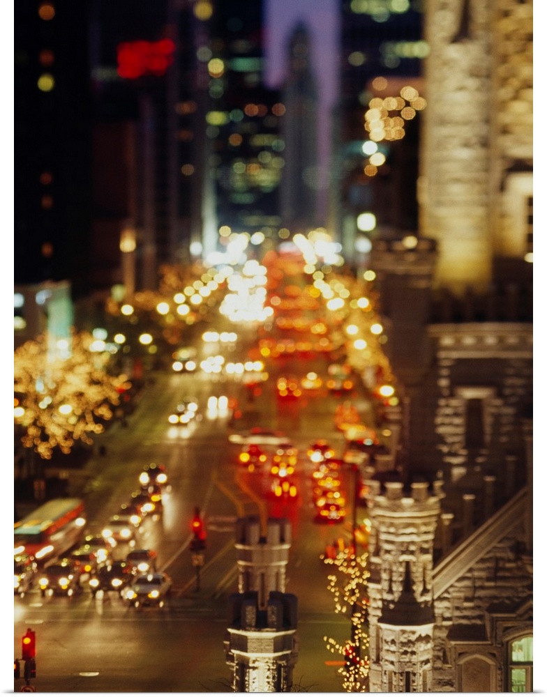 Vertical panoramic photograph of busy street lined with tall buildings that are lit up in the night sky.