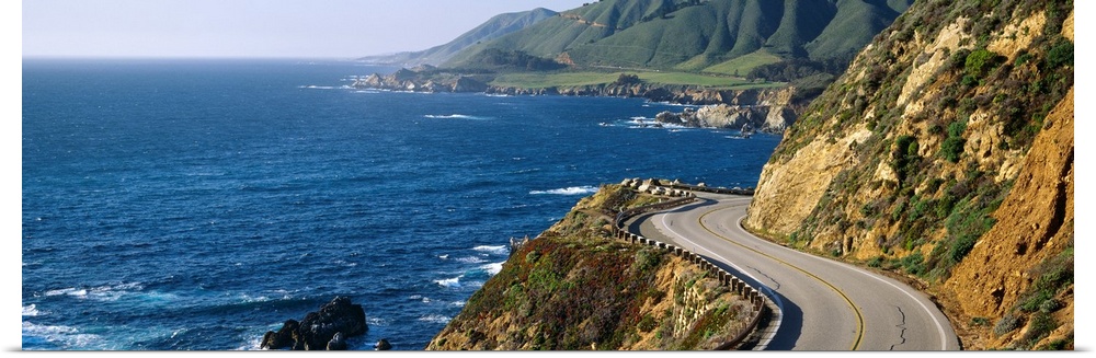 Big, panoramic landscape photograph of curving Route 1 on a hillside, along the coast of Big Sur, California.