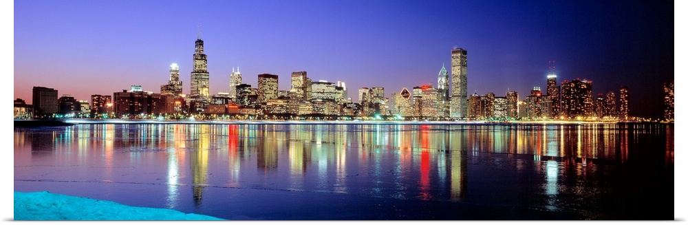 Panoramic photographic canvas of a cityscape illuminated with colored lights reflected perfectly onto the water at dusk.