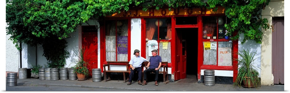Panoramic picture snapped of two men as they sit on a bench outside a bar in Ireland. The front of the bar is lined with b...