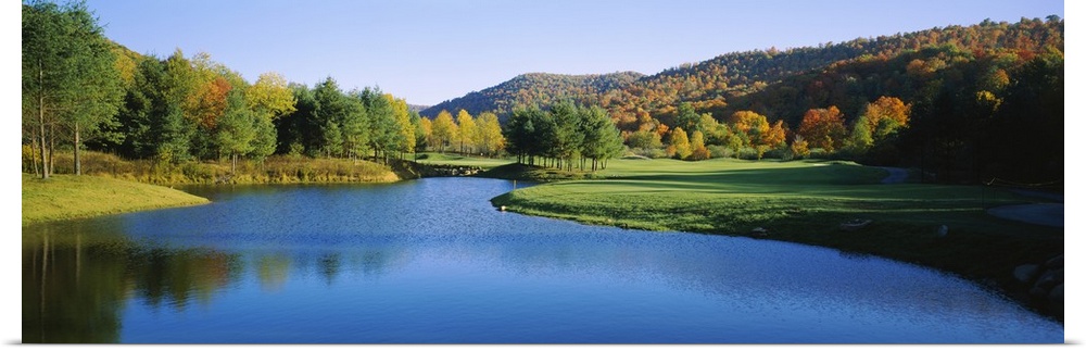 Long horizontal canvas print of a golf course with a lake in the middle and fall foliage on rolling hills in the background.