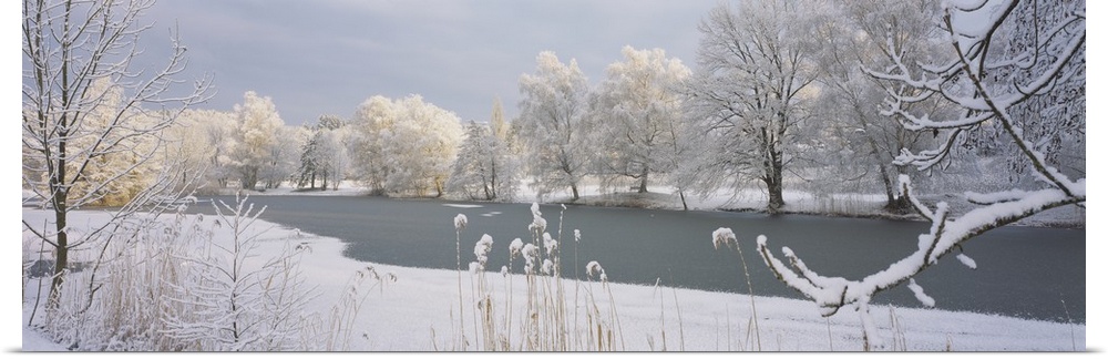 A frozen lake is photographed and surrounded by snow covered trees and land.