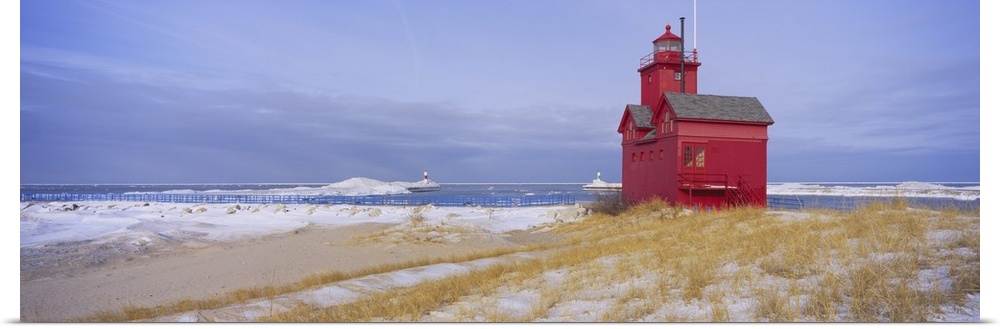 Lonely red light house on the edge of the water on a snowy beach, standing out against the pale cloudy sky.