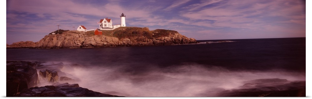 Panoramic photograph of Nubble Lighthouse on top of a rocky hillside, along the coast of York, Maine, while coastal waters...