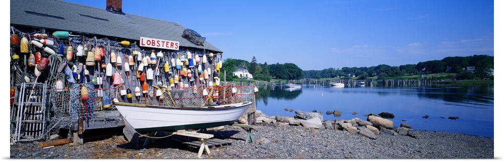 Panoramic photograph taken of a lobster shack with small buoys lining one side of it that sits on the edge of a body of wa...