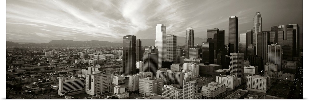 Panoramic photograph of Los Angeles, CA skyline with mountains in the distance and clouds overhead.