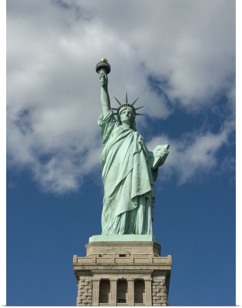 Vertical, low angle photograph on a big canvas, looking up at the Statue of Liberty against a blue sky with thin white clo...