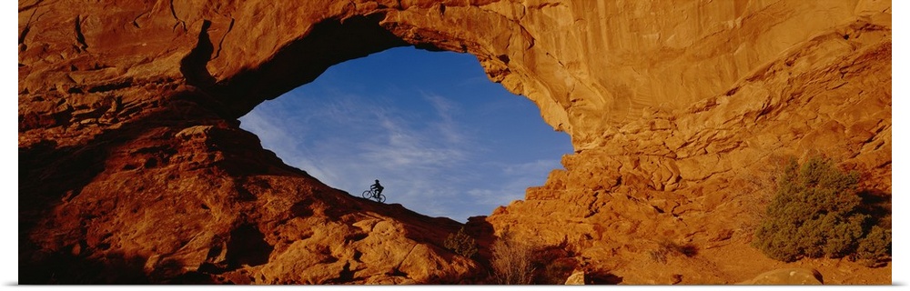 Giant, horizontal, wide angle photograph of the side of a mountain in Utah.  There is a mountain biker in an eye shaped op...