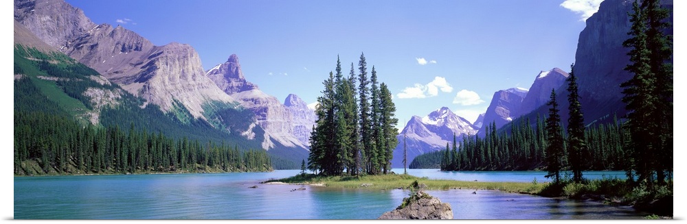 A small island with pine trees in the center of a clear turquoise lake, surrounded by rocky mountains.