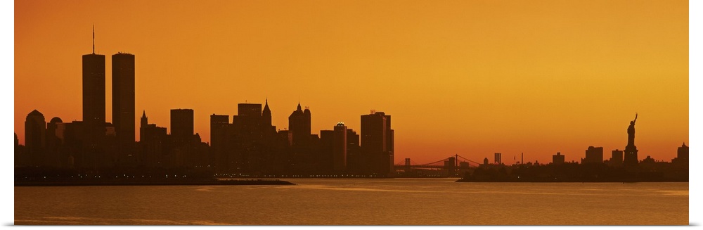 Panoramic photo of the silhouette of the NYC cityscape against a warm sunset.