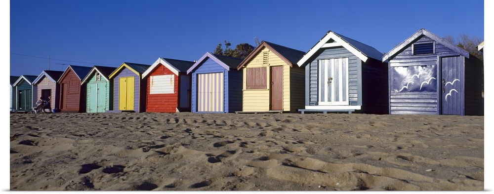 A row of colorful huts are photographed lining the sandy beach.