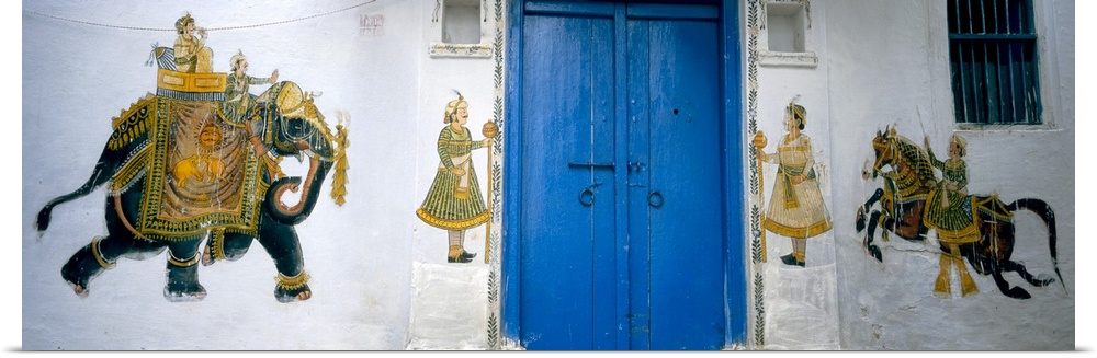 Panoramic photograph taken of a mural painted on either side of bright blue doors. The mural consists of a large elephant ...