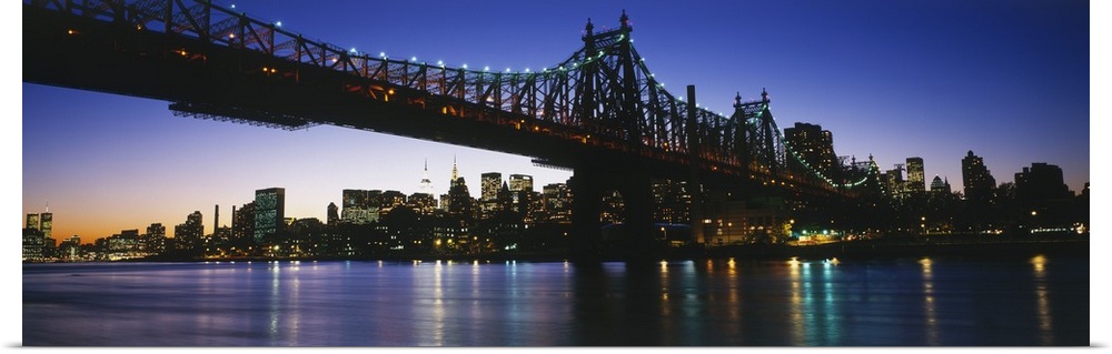 Big, panoramic photograph of the 59th Street Bridge, lit at night, the New York City skyline in the background.
