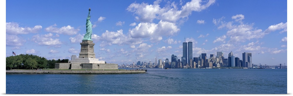 Panoramic picture taken from a distance of the NYC skyline with Ellis Island and the Statue of Liberty to the left.