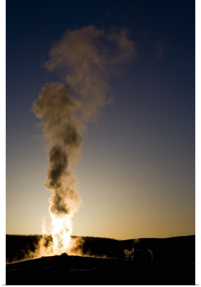 Portrait photograph on a big wall hanging of steam rising into the air as Old Faithful erupts as the sun sets.