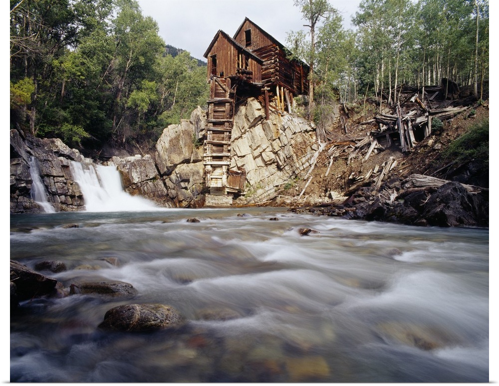 Photograph of old log cabin sitting on top of rocky hill with rushing stream below.
