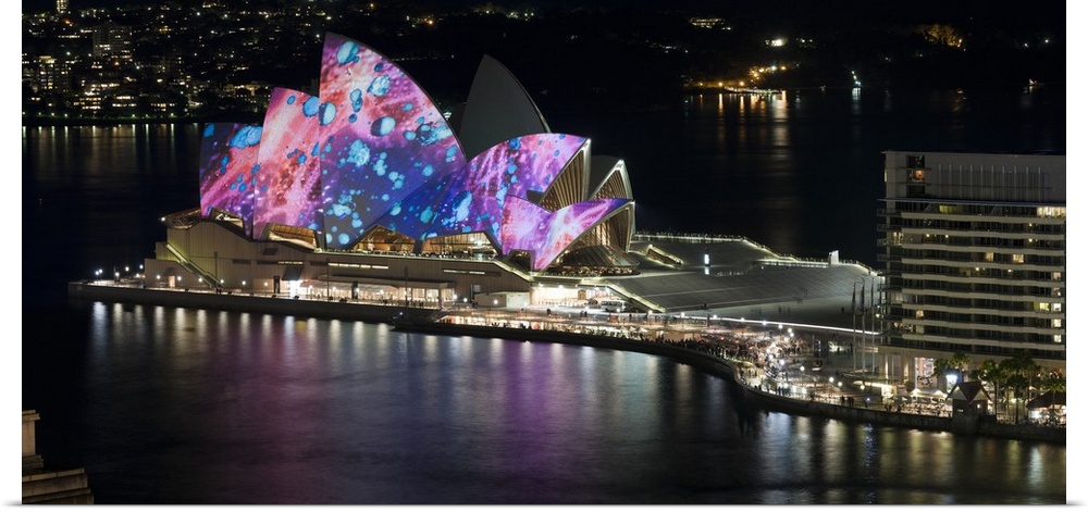 This landscape photograph shows colorful lights and illustrations projected on to this landmark building in a harbor.