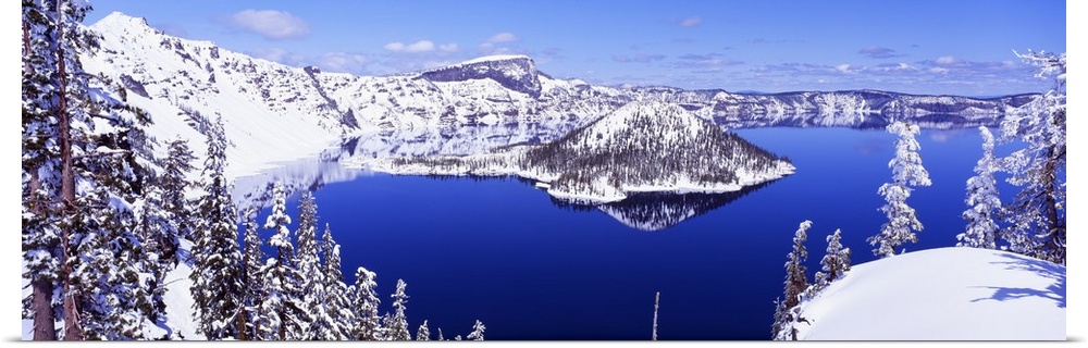 Wide angle shot taken of Crater lake looking out toward snow covered mountains and pine trees.