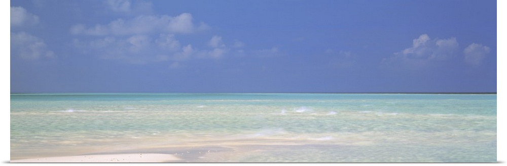 Panoramic canvas photo of a clear ocean meeting a sandy beach.