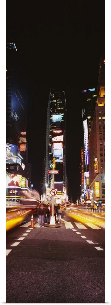 This vertical time lapsed photograph shows the blur of motion created by cars driving through Time Square beneath the mass...