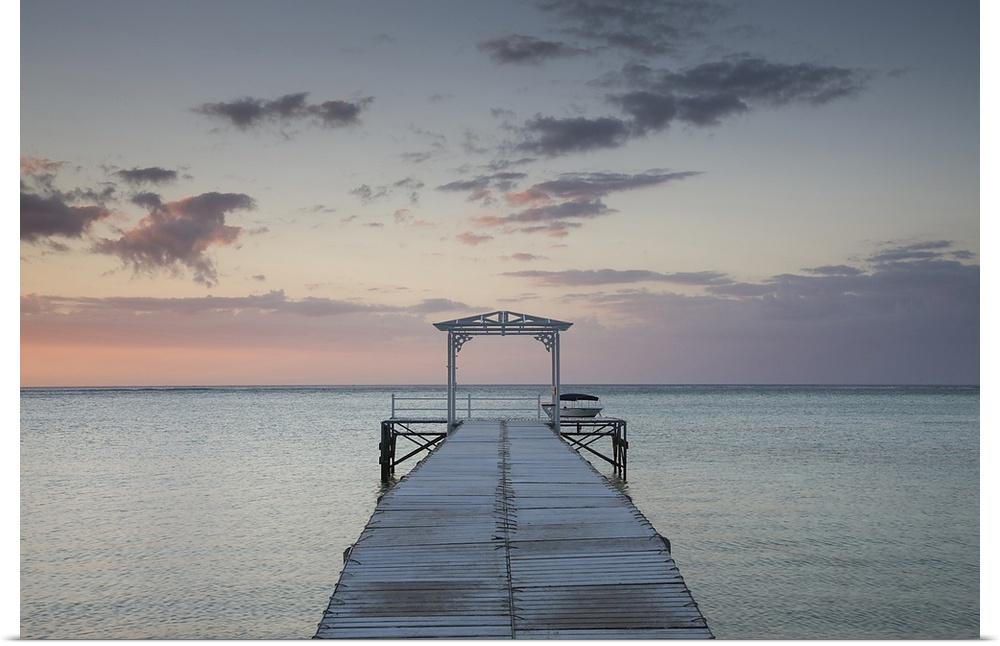 Photograph of wooden dock stretching into ocean at sunset under a cloudy sky.