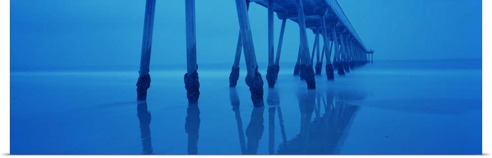 Photograph taken underneath a long pier that stretches far out into the ocean.