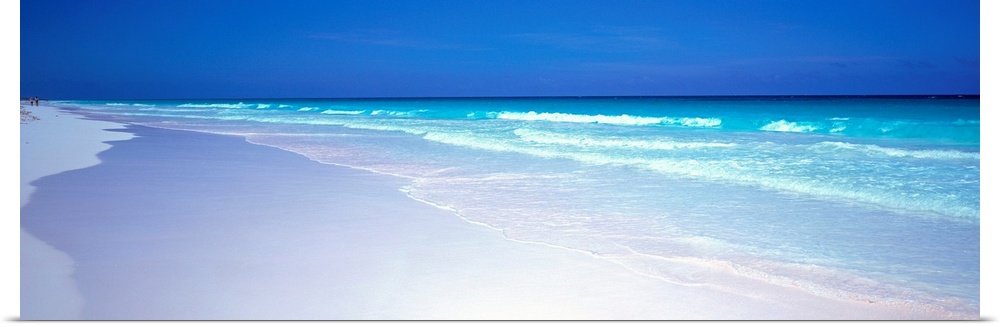 A panoramic wall art picture of a tropical beach with flawless sand and a clear horizon as waves wash up on the shore.