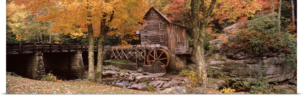 Panoramic photograph of old stone bridge leading to water mill located in a fall forest.