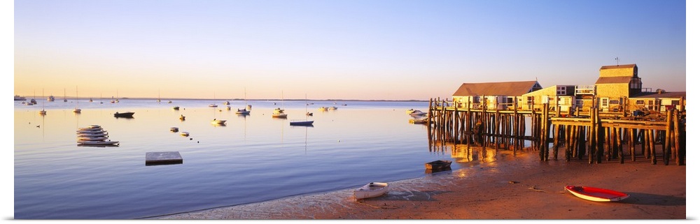 Picturesque panoramic photograph of a beach and small pier in Provinetown, Massachusettes. Small boats float in the ocean ...