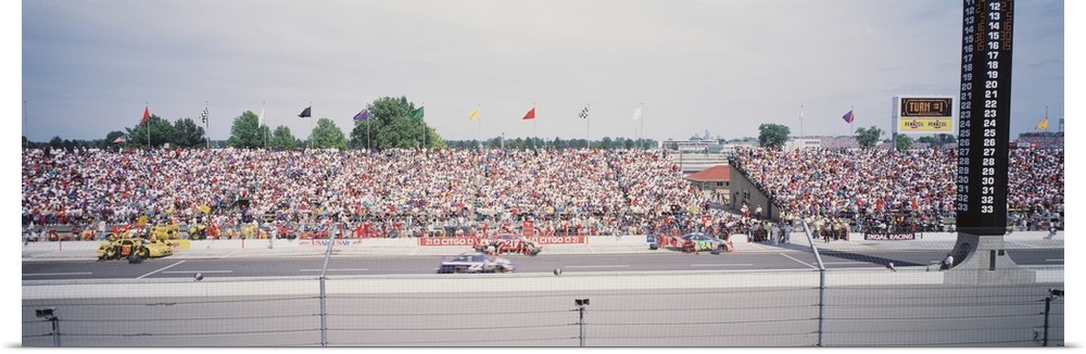 Panoramic photograph taken inside a race track. Cars are shown speeding along with a packed crowd in the stands.