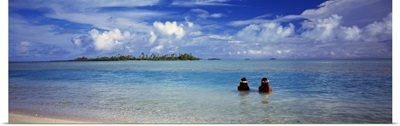 Rear view of two native teenage girls in lagoon water looking toward horizon, Aitutaki, Cook Islands