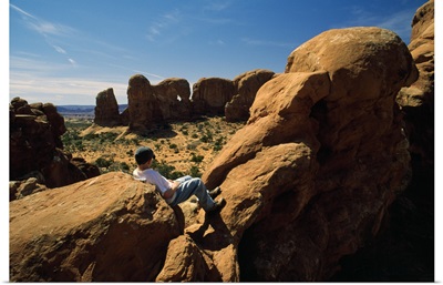 Rear View Of Young Boy Resting Against Boulder