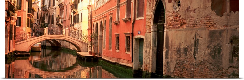 Panoramic photograph focuses on buildings and bridges following a canal in Venice, Italy.  Located on the surface of the w...