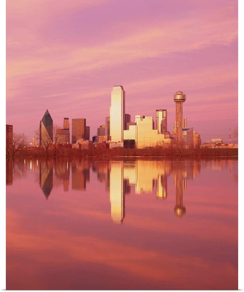 During sunset, the Dallas skyline is photographed from across a body of water that it reflects in.