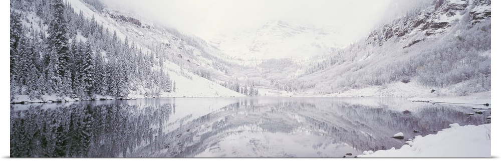 Large panoramic photograph of a lake with the reflection of the snow covered trees and mountain in the water.