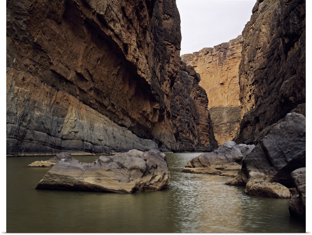 Photo print of a rugged canyon with water flowing by big rocks at the bottom.
