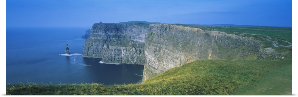 Wide angle photograph of curving, large rock formations of the Cliffs of Moher, leading into the water in County Clare, th...