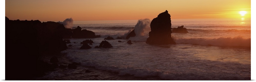Panoramic photo on canvas of rock formations on a beach with waves breaking on the shore at sunset.