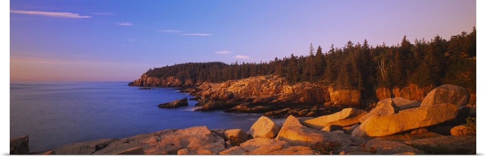 Wide angle photograph of the rocky shoreline, surrounded by trees at sunset, in Acadia National Park, Maine.