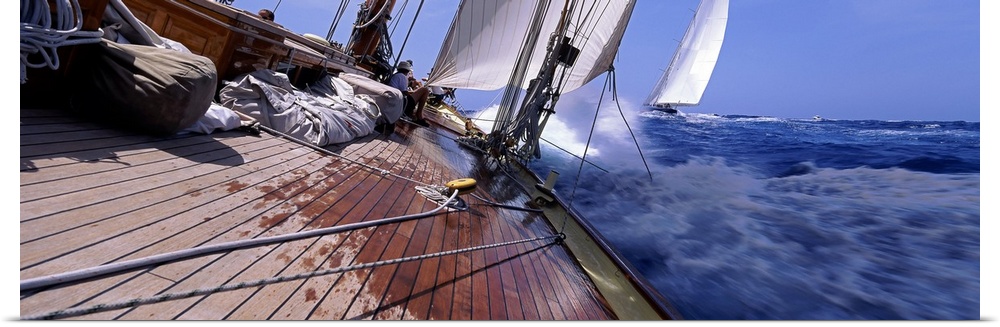 View from a boat of sails and cords stretched over the deck with ocean water splashing against the bow as it makes a sharp...