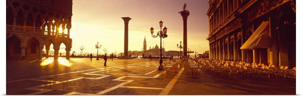 Sun setting on the Piazza di San Marco, its light shining through the historic pillars of the surrounding buildings.