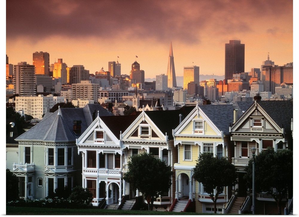 Photograph of pastel colored row houses with city skyline in the background at dusk.