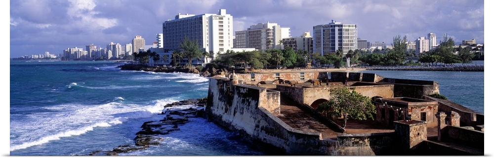 Panoramic photograph of San Jeronimo Fort on the waters of San Juan, the city skyline in the background, in Puerto Rico.