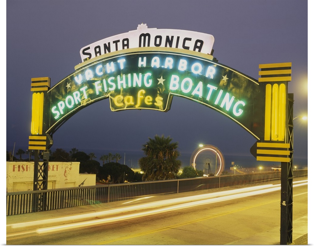 Long exposure shot of a lit up Santa Monica Pier sign at night as traffic headlights go by and the Ferris wheel spins in t...