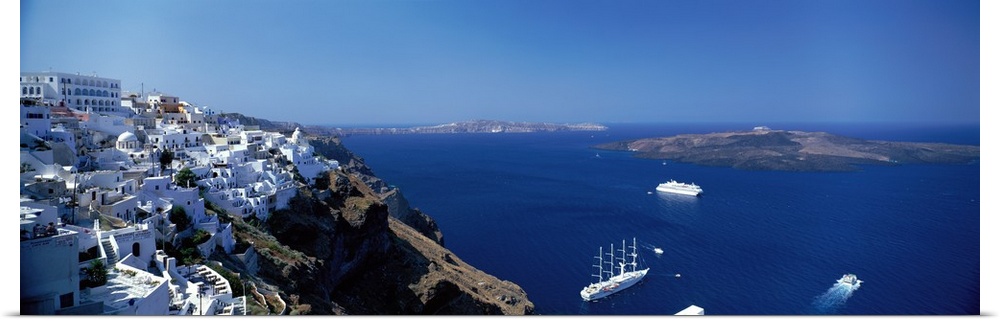 Scenic photo of white houses sitting on the mountain Cliffside in Santorini, Greece with blue ocean water down below.