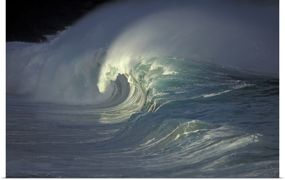 Photograph of a wave curling and crashing as it nears shore with sea mist spraying behind it.